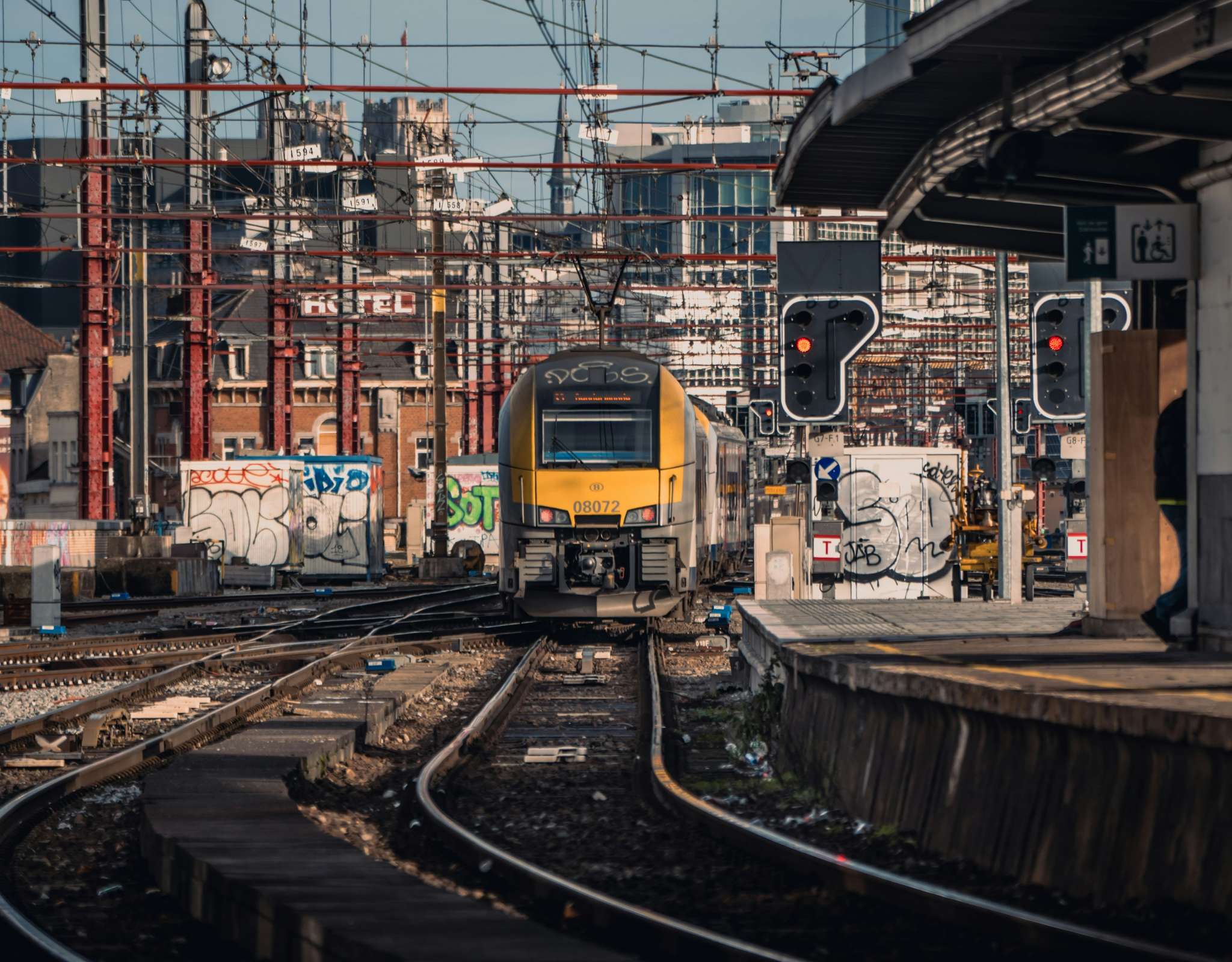 Vue frontale d’un train SNCB jaune dans un nœud ferroviaire avec signaux.