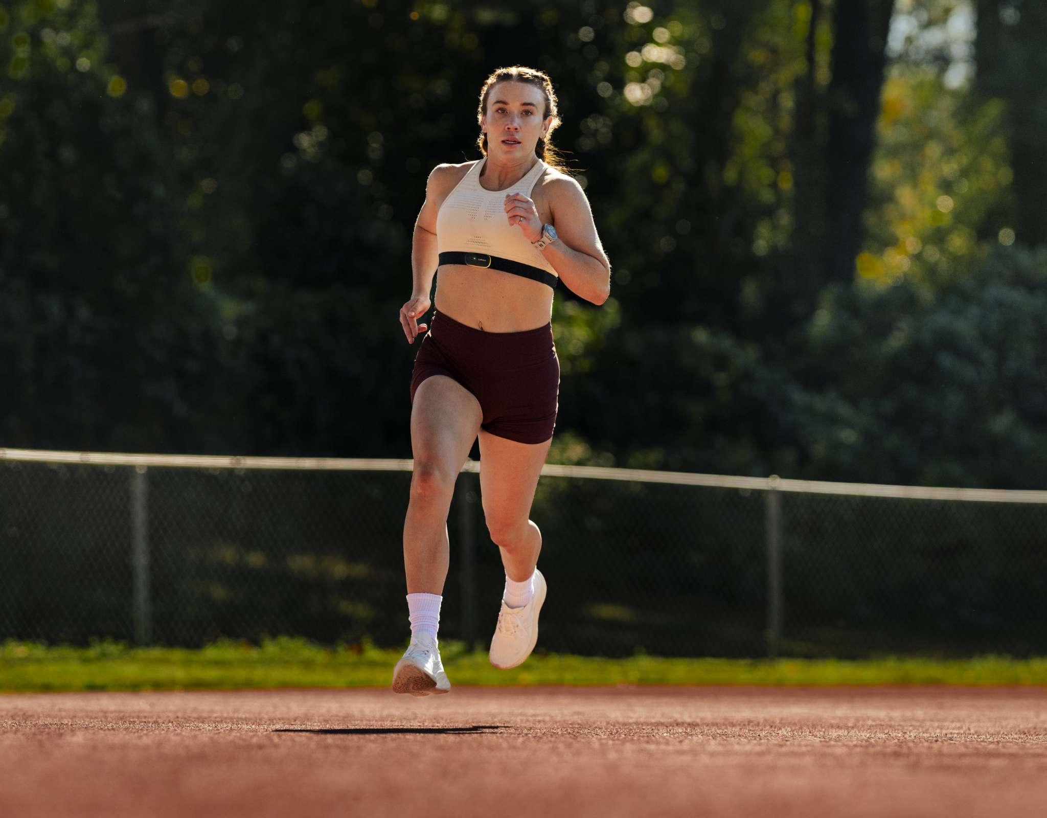 Femme courant sur une piste d’athlétisme avec montre de sport en plein air.
