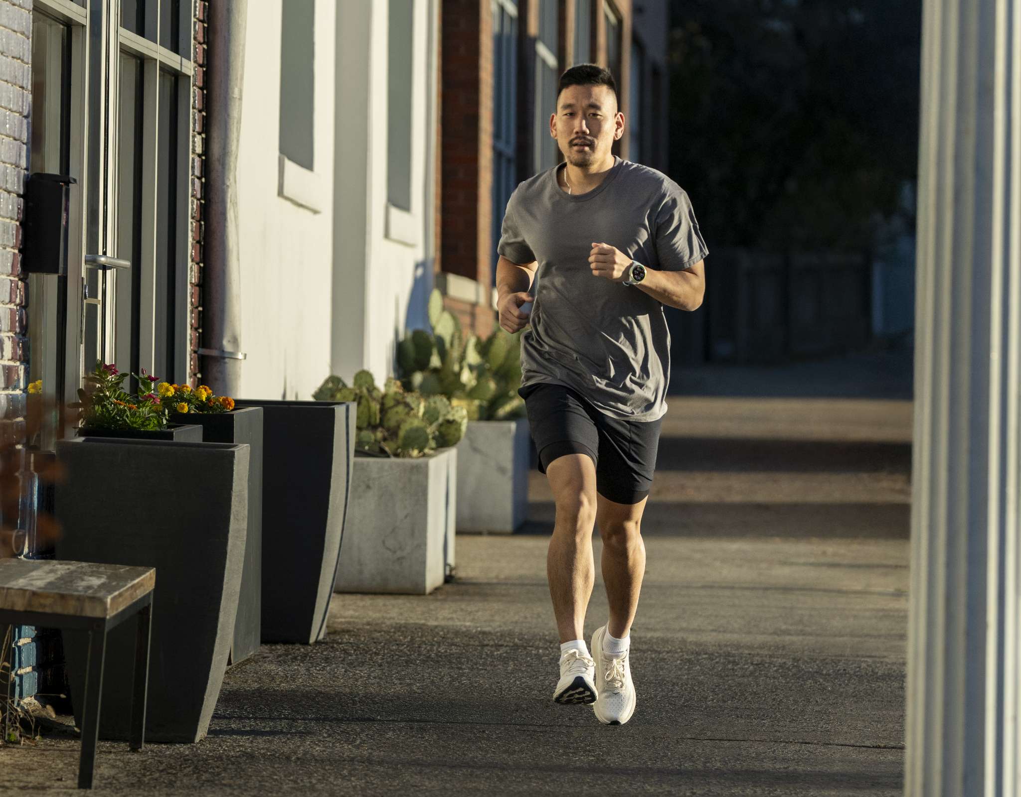 Homme courant sur un trottoir en ville avec montre de sport et tenue sportive.