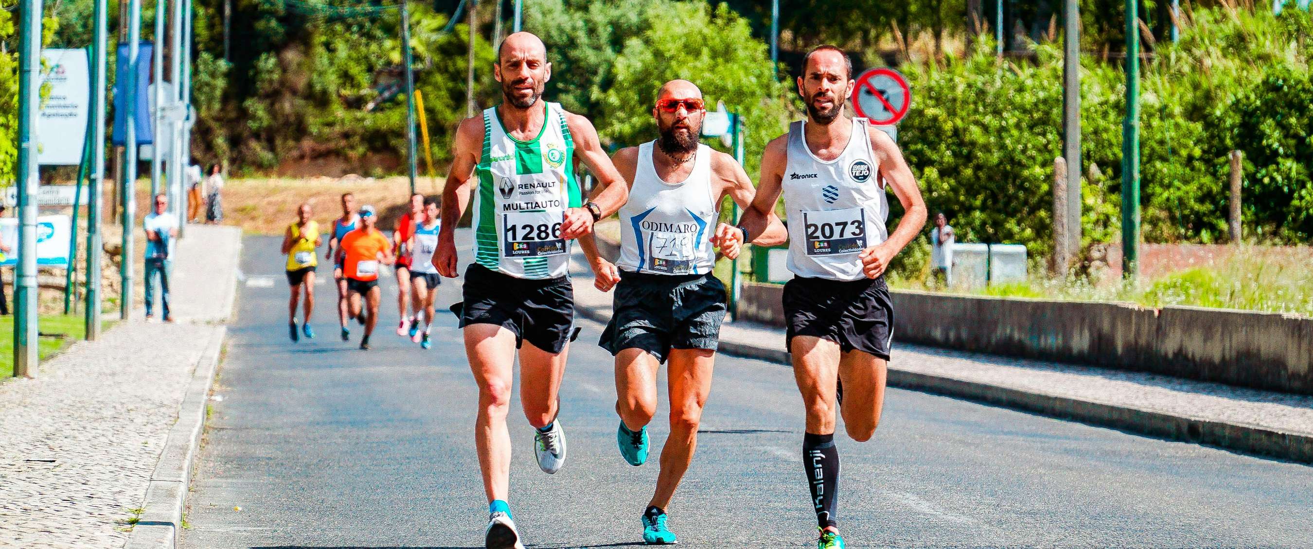 Drie mannelijke hardlopers in koppositie tijdens een marathon, met de rest van het peloton op afstand.