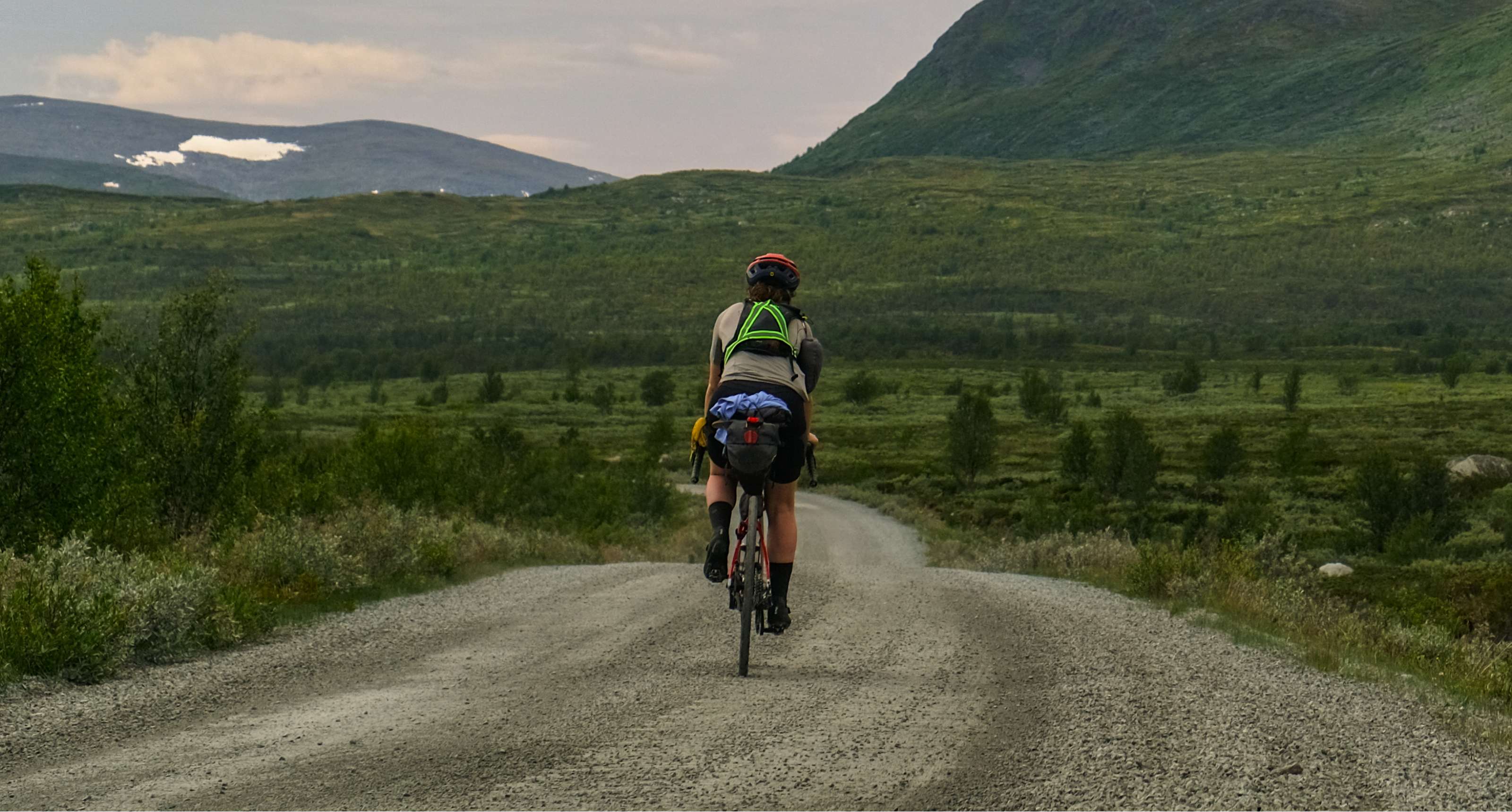 Une cycliste avec une grande sacoche de selle roule sur une piste de gravier dans une vallée verdoyante.