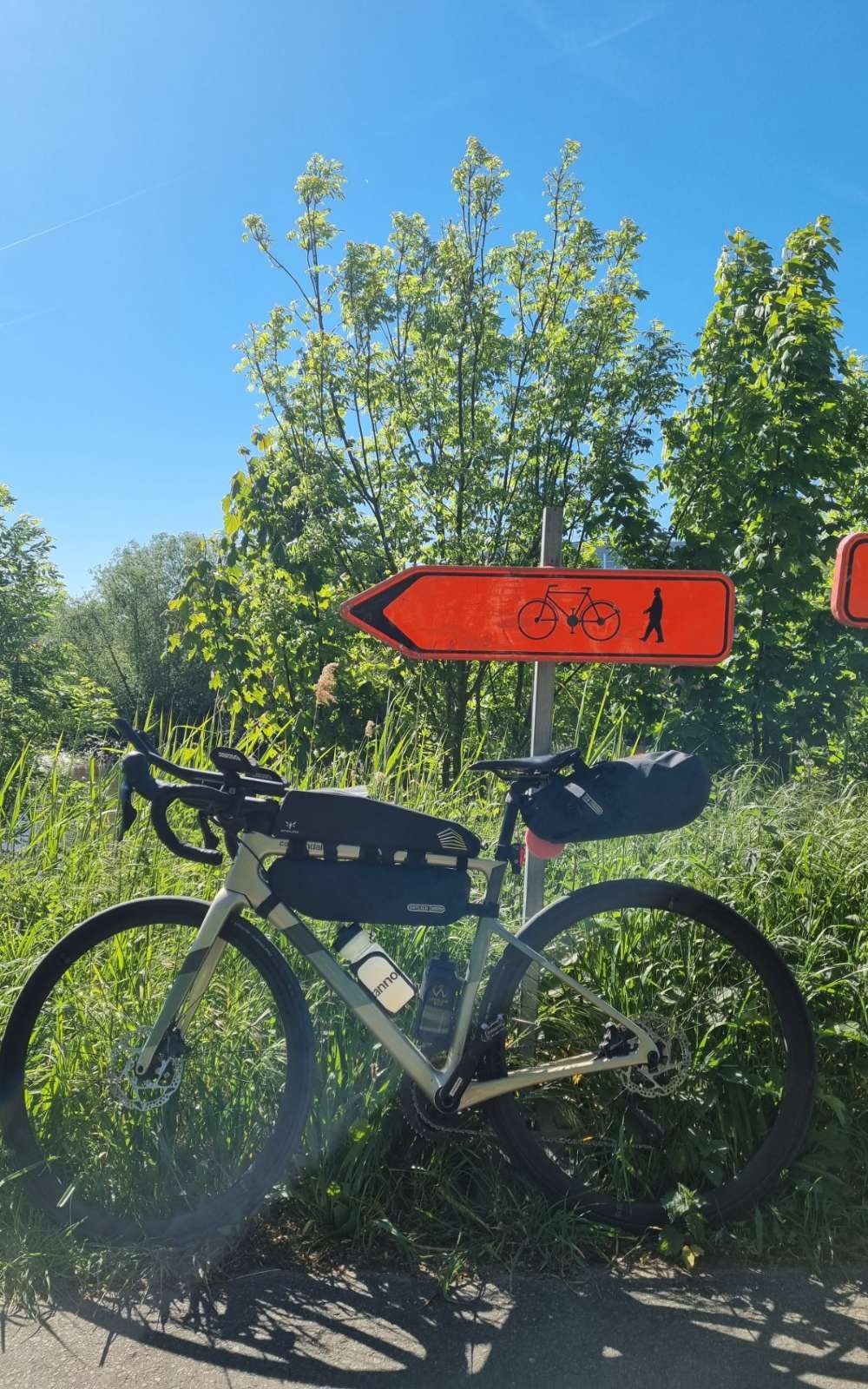 Un vélo avec sacoches de cadre et de selle dans l'herbe sous un panneau rouge pour cyclistes et piétons.