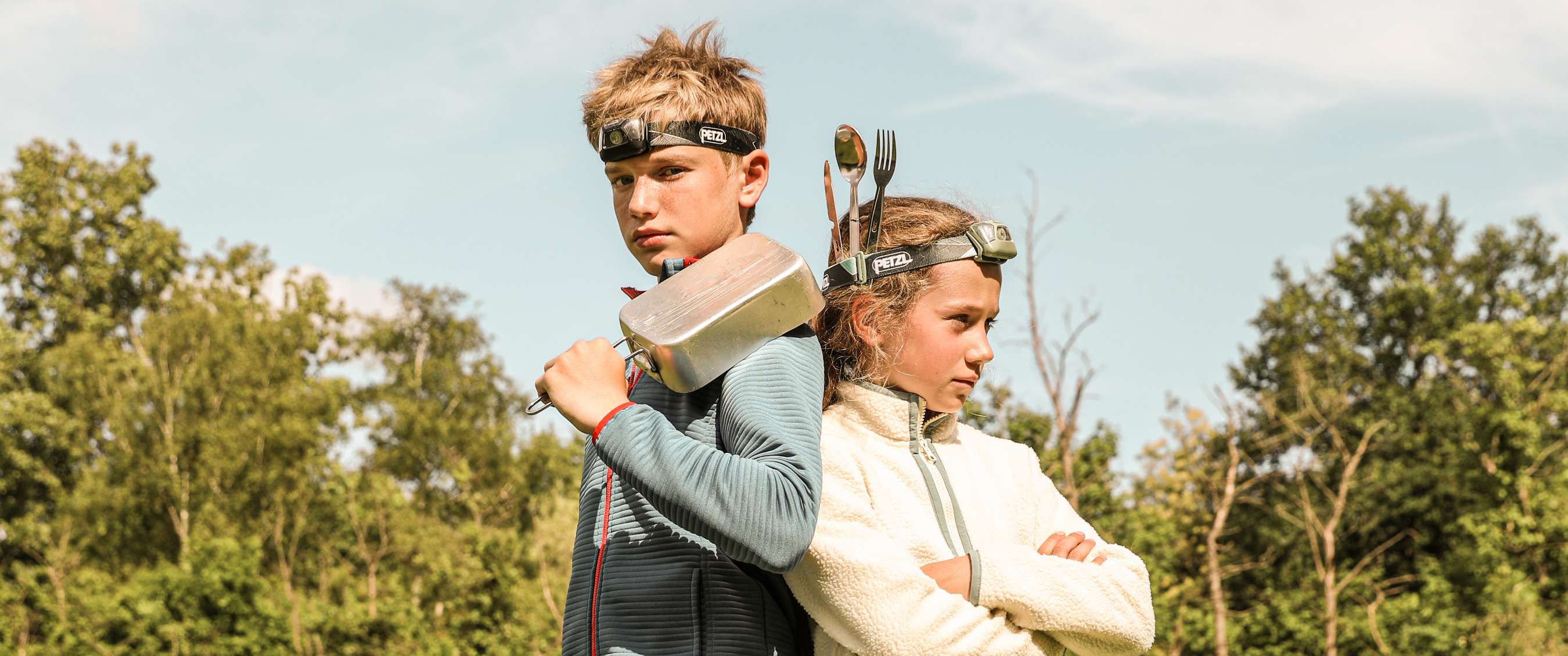 Deux enfants avec lampes frontales Petzl posent dos à dos dans la nature.