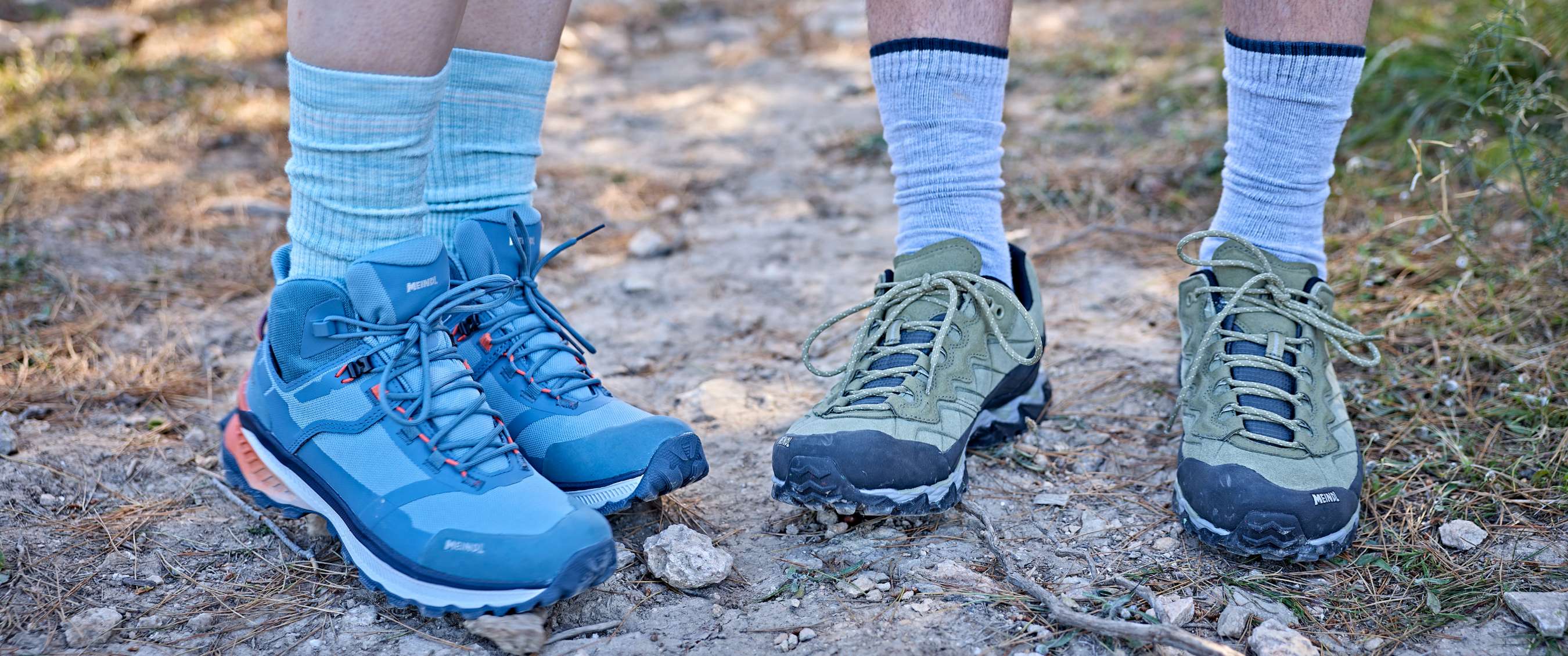 Deux paires de chaussures de randonnée avec chaussettes sur un sentier sec.