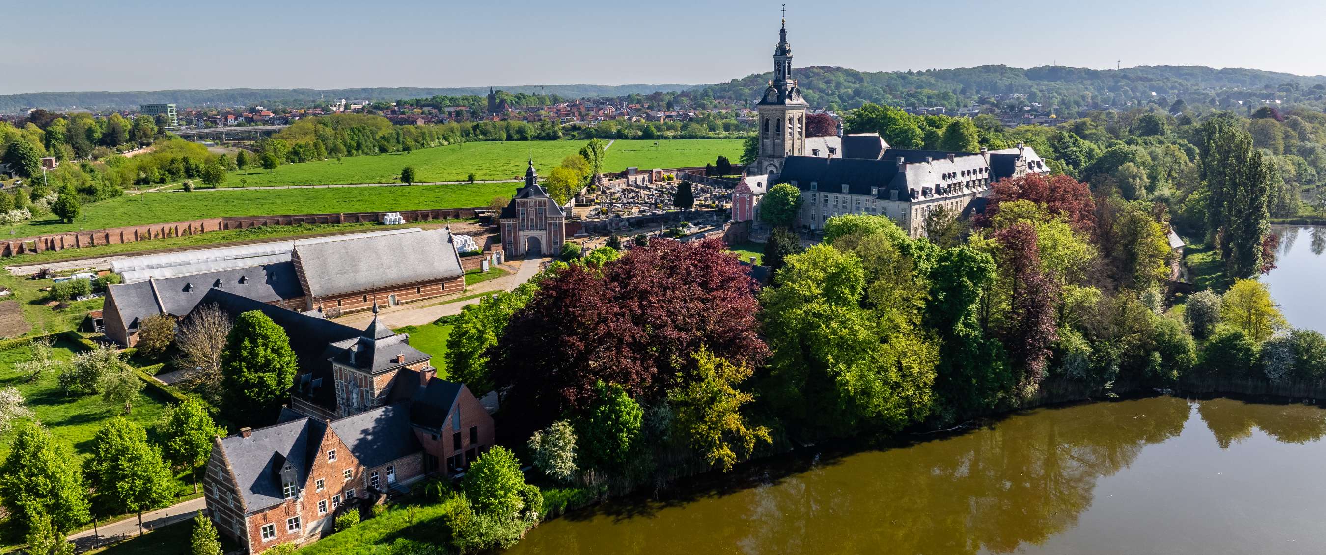 Vue aérienne d’une abbaye au bord d’une rivière avec arbres et champs près de Louvain.