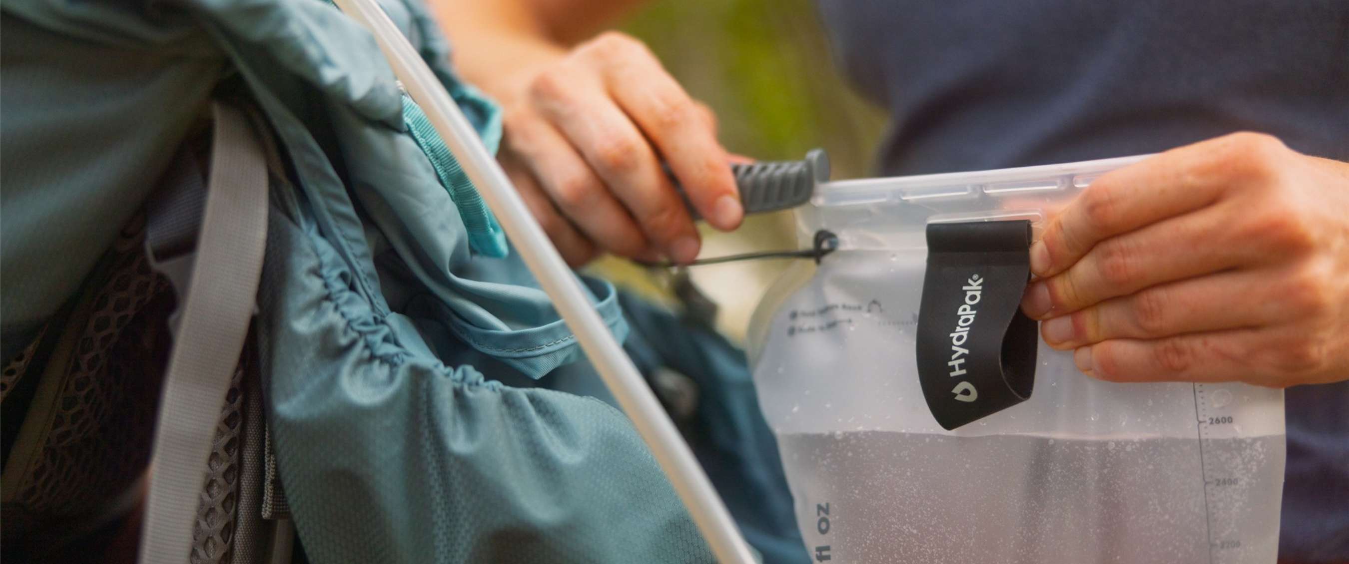 Des mains remplissent une poche à eau HydraPak dans un sac à dos avec tube visible.