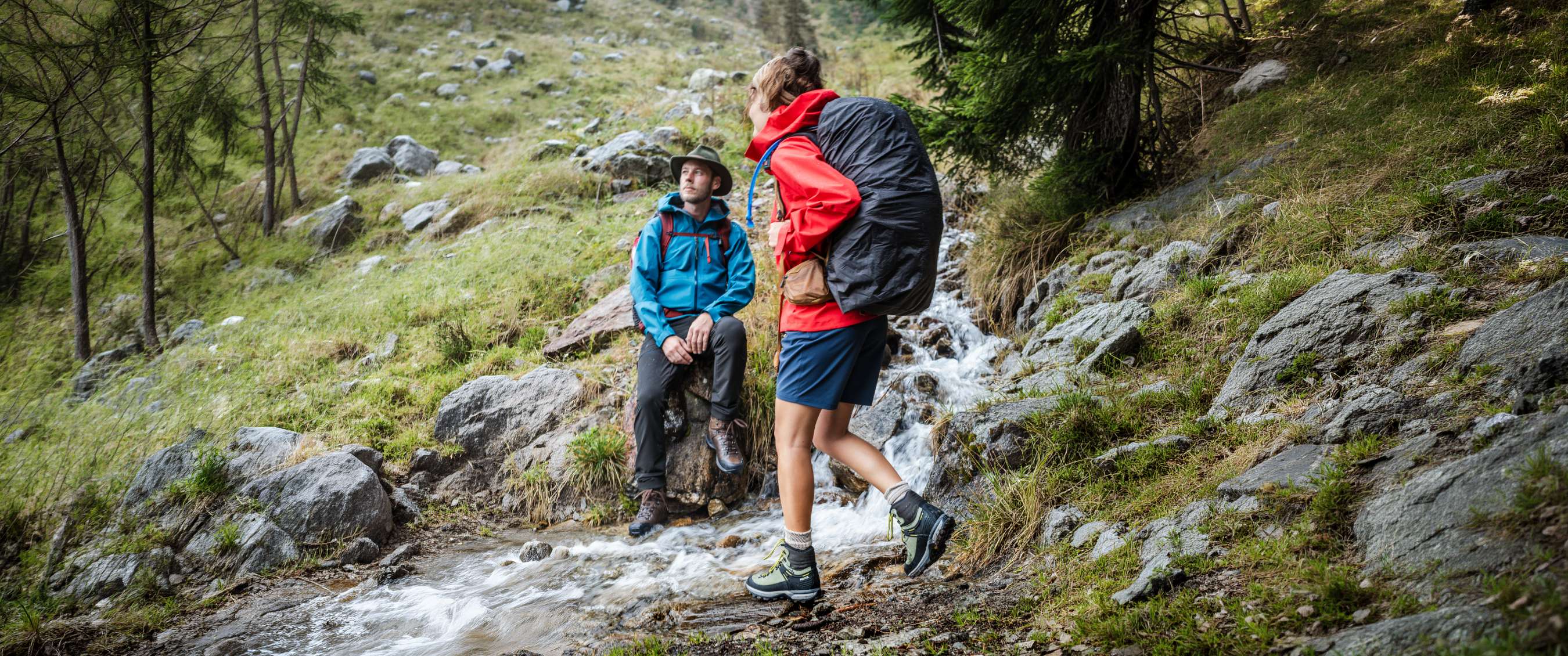 Des randonneurs en chaussures montantes près d'un cours d'eau parmi les rochers et les conifères.