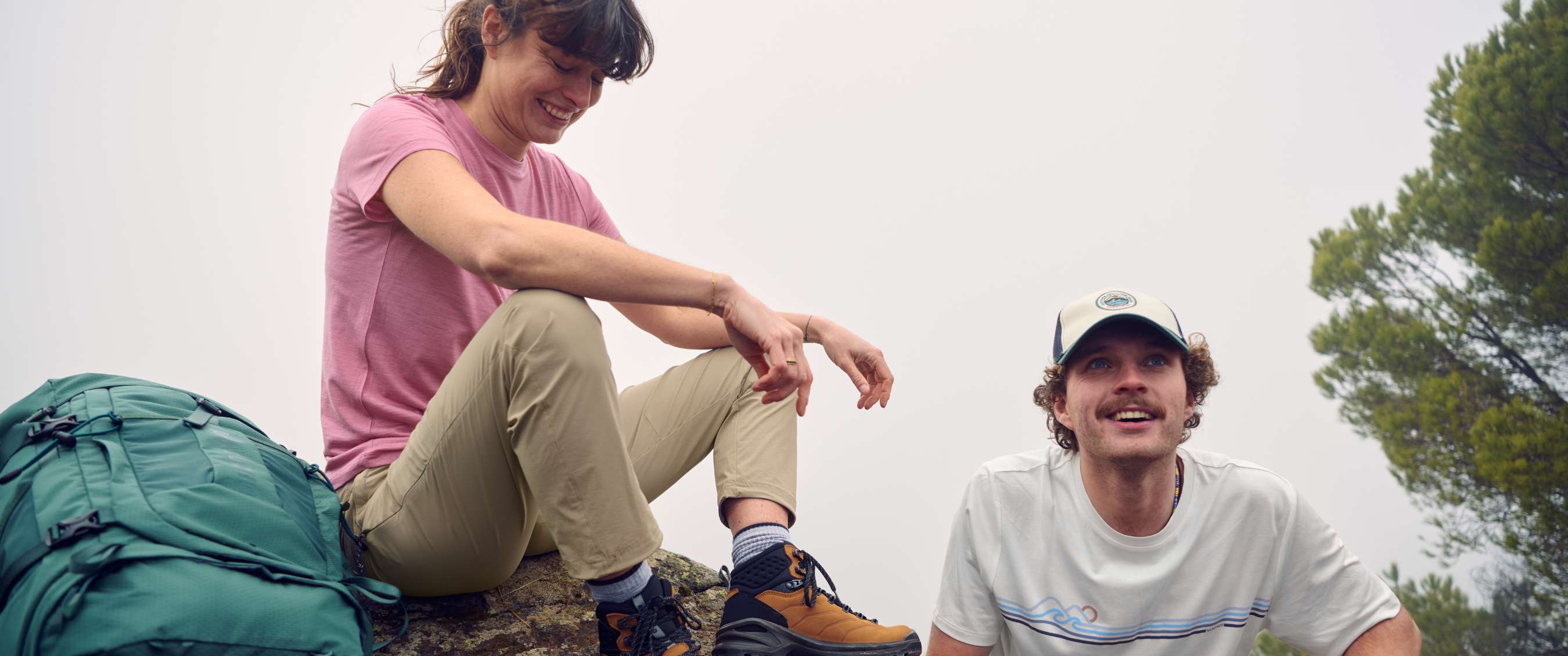 Une randonneuse en chaussures de marche brunes est assise près d’un randonneur avec casquette.