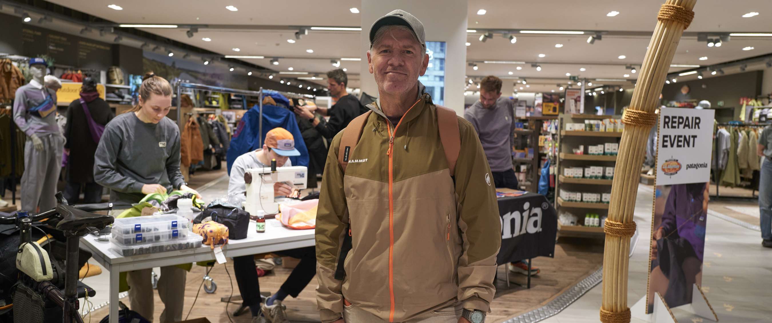 Homme dans un espace de magasin avec table de réparation et panneau visible REPAIR EVENT.