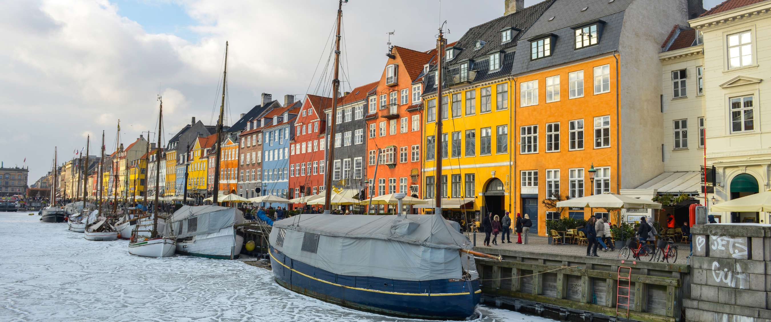 Façades colorées au bord de l’eau et bateaux sur un canal partiellement gelé.