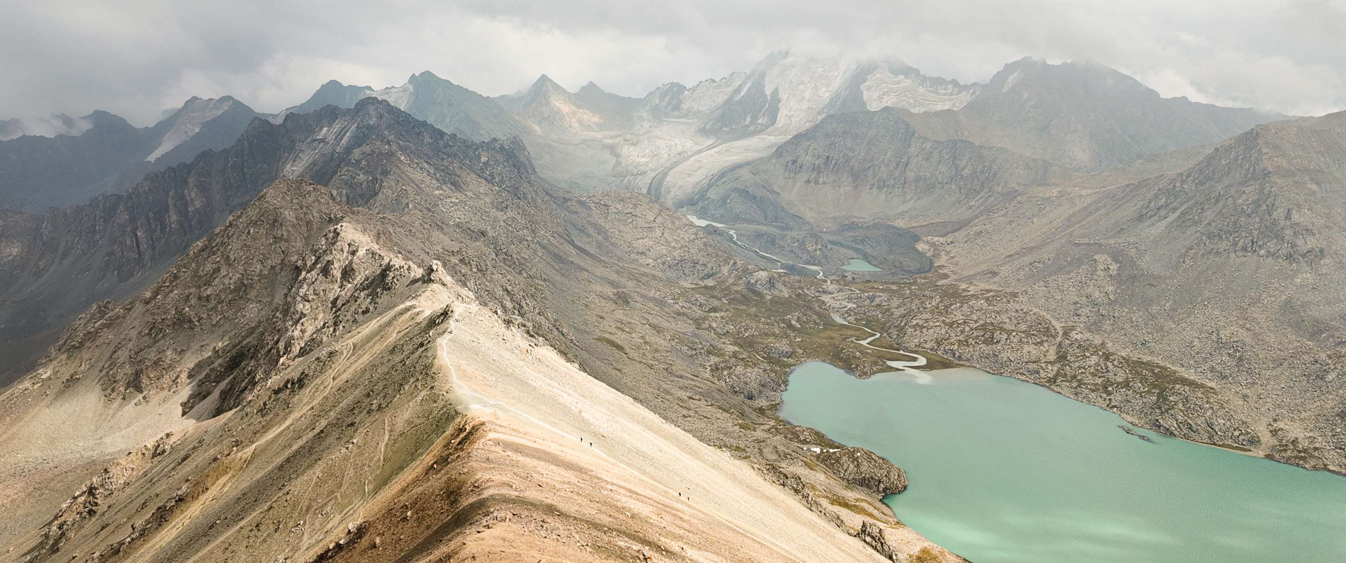 rête rocheuse avec lac turquoise et glacier dans un vaste paysage de haute montagne.
