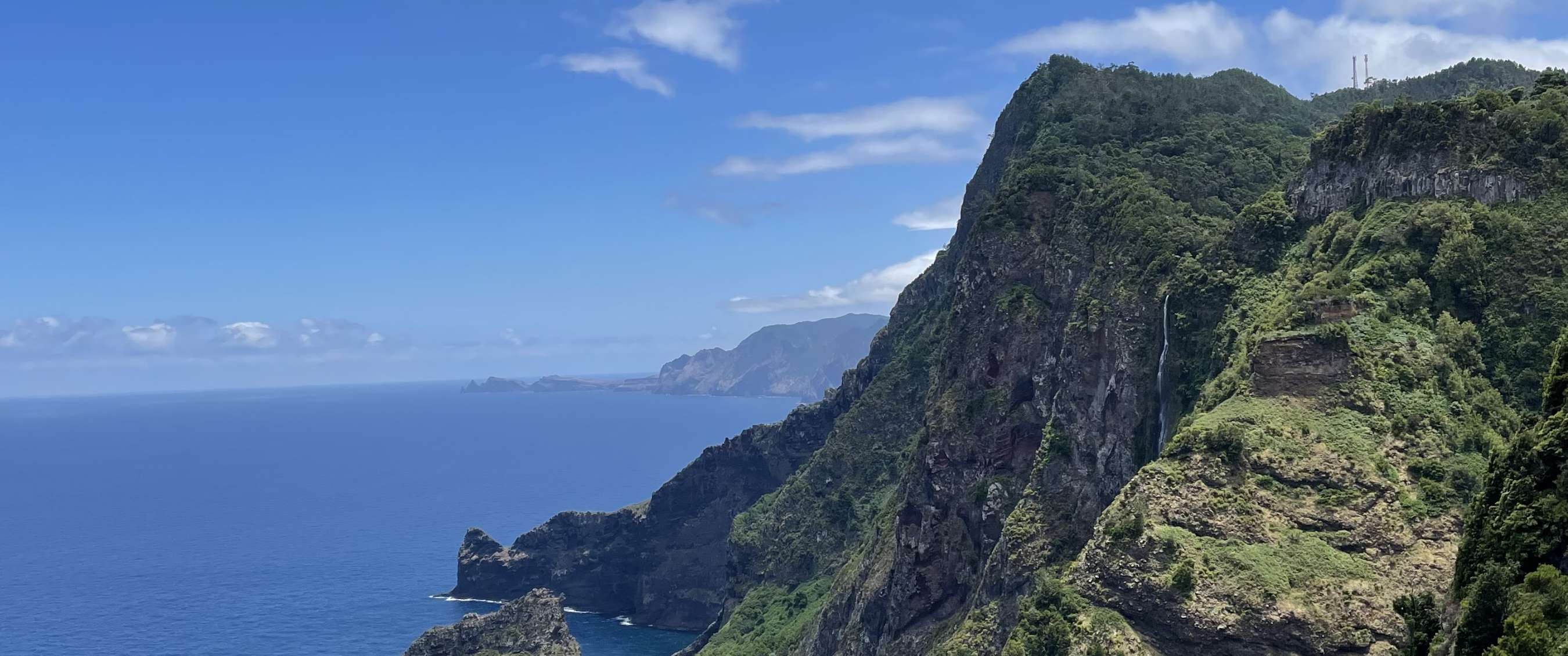 Côte rocheuse avec montagnes verdoyantes, océan et ciel bleu clair