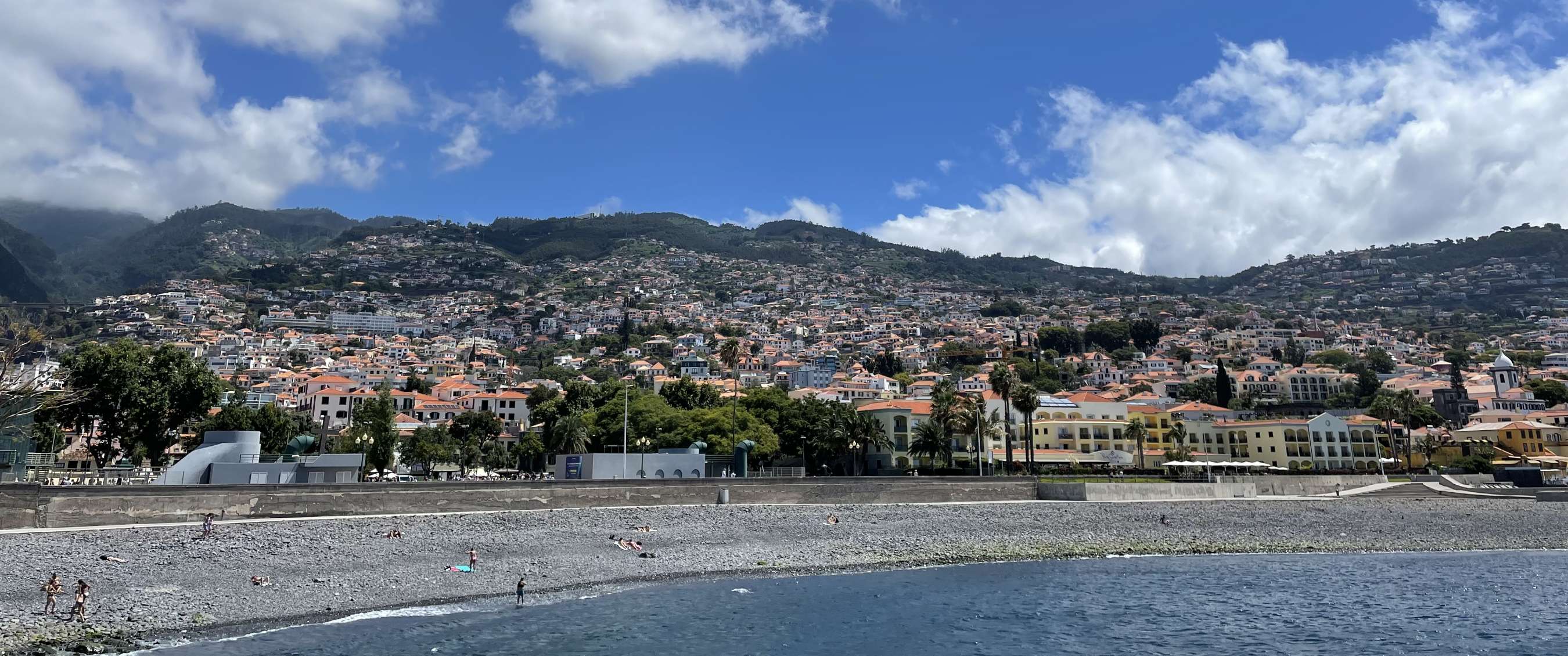 Ville côtière avec plage de galets, mer et maisons sur des montagnes vertes