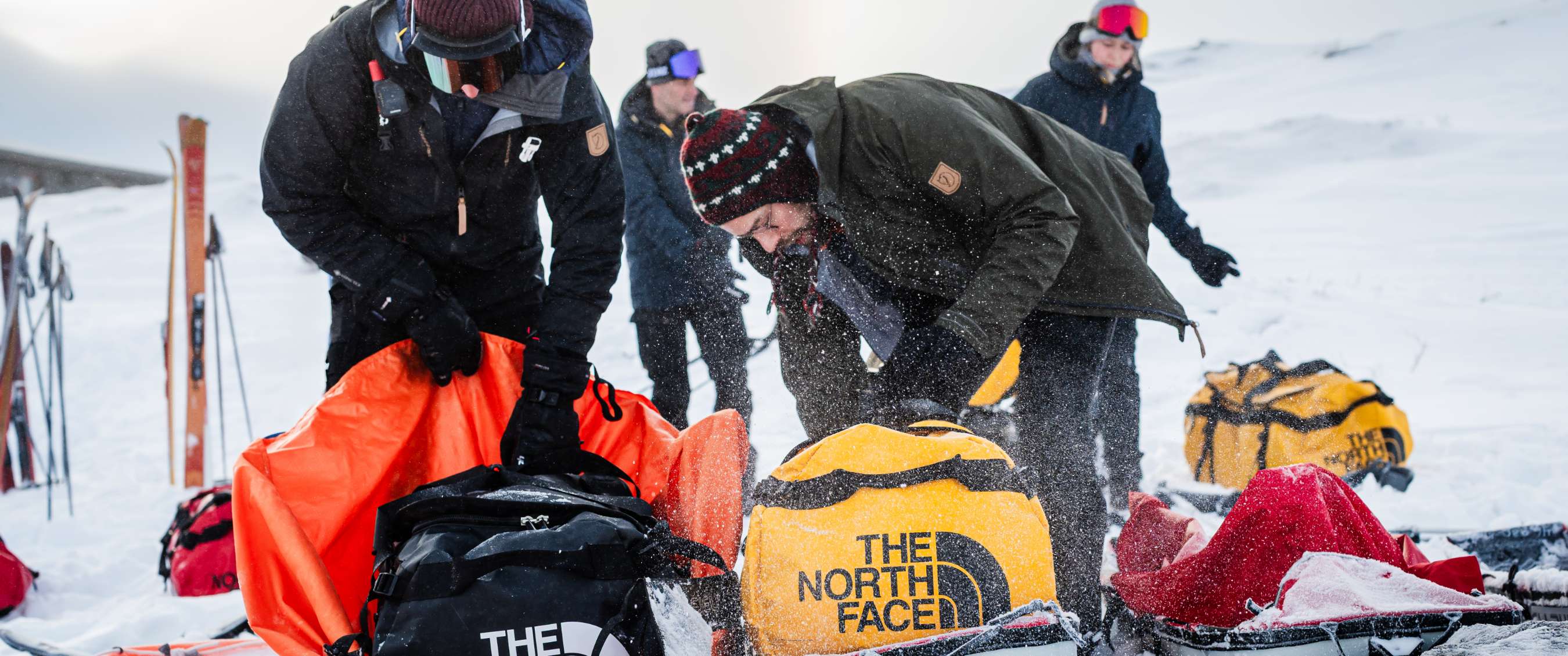 Personnes déballant des sacs duffel The North Face dans un paysage enneigé.