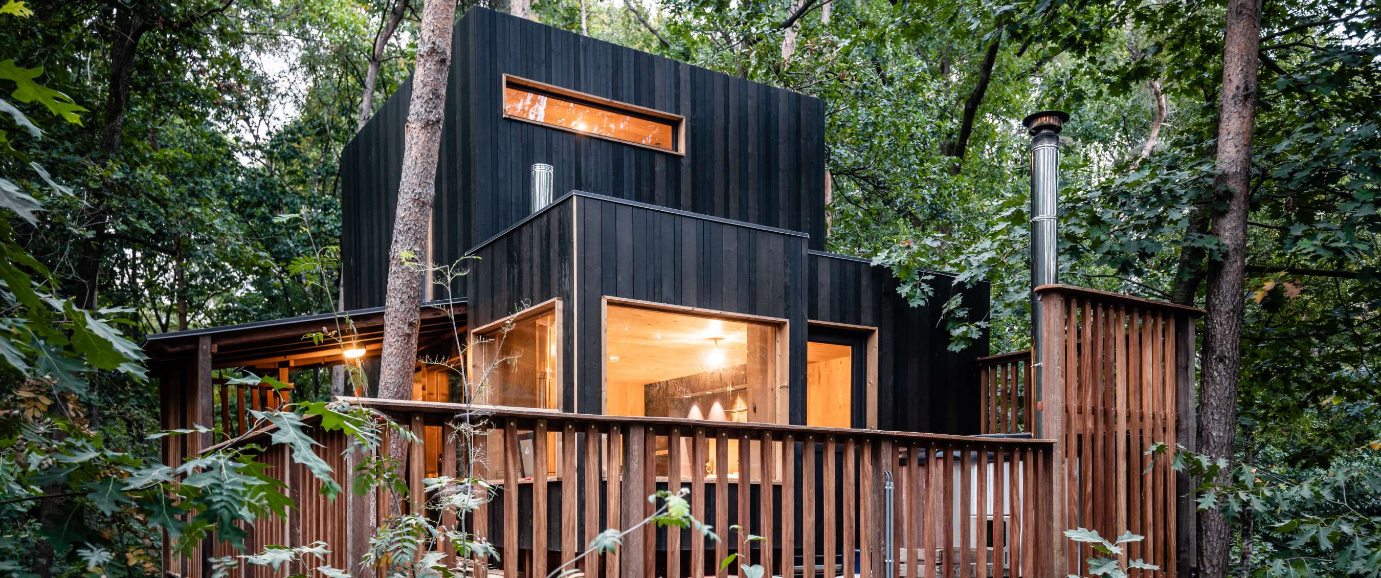 Cabane en bois noir avec grandes fenêtres et balustrade en bois
