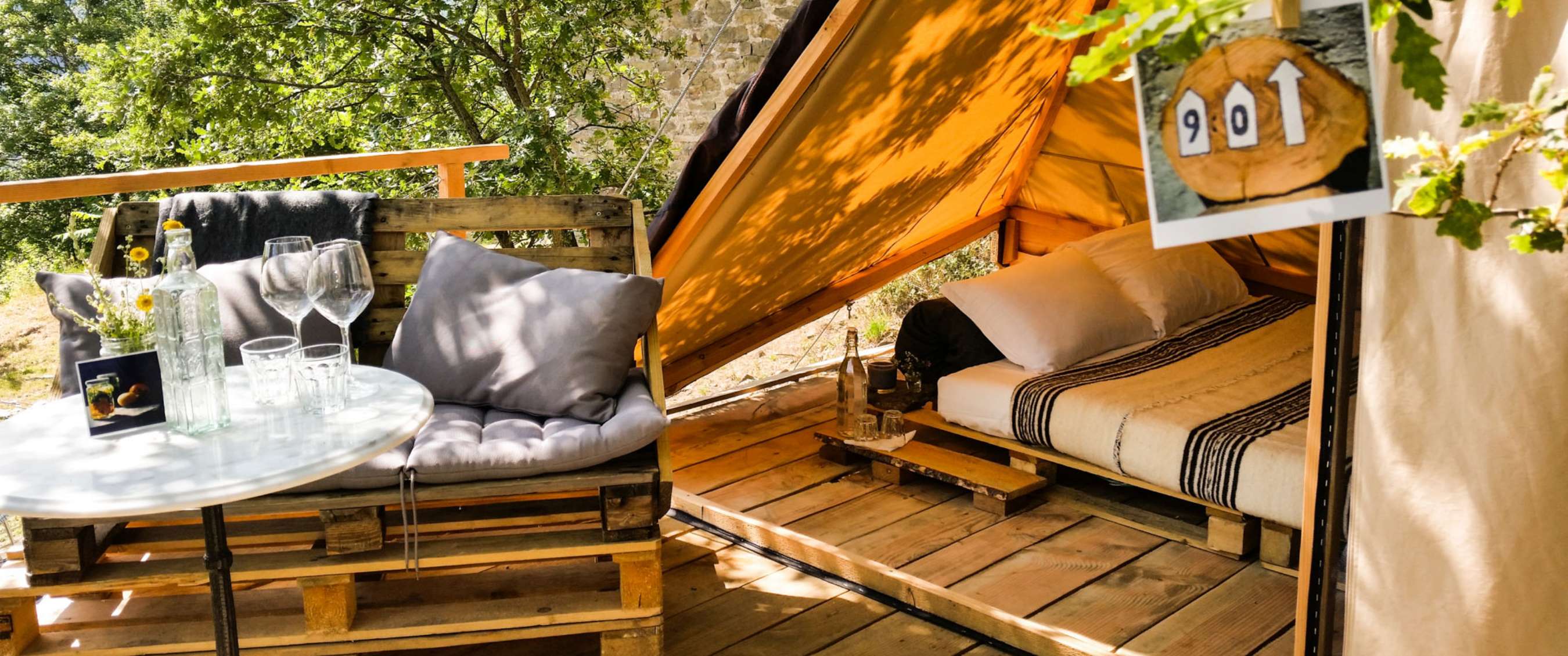 Deux images : coin extérieur avec table, verres et coussins dans un cadre verdoyant ; intérieur d’une tente glamping avec lit double et sol en bois.