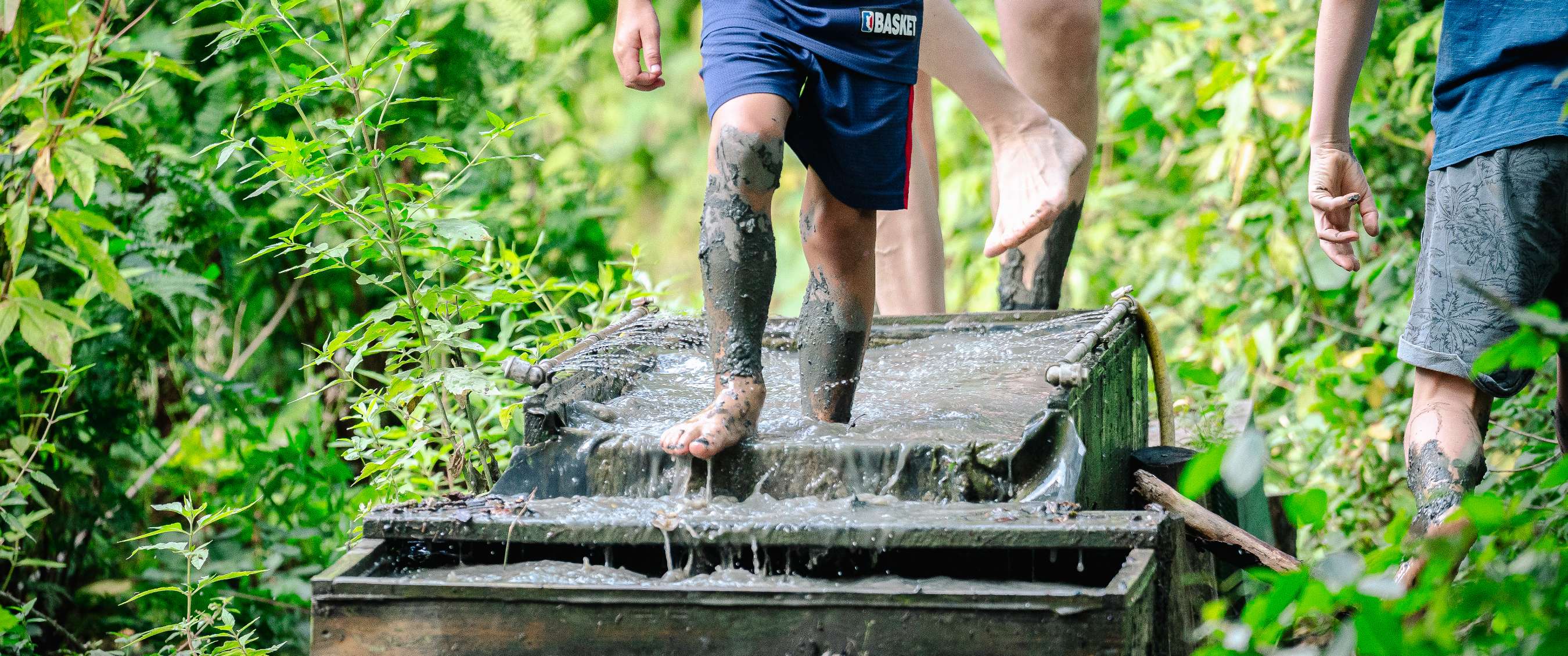Un enfant marche pieds nus dans un bassin boueux au cœur d’un environnement boisé.