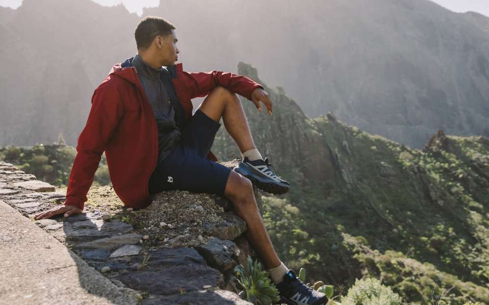 Personne en chaussures de randonnée assise sur un mur rocheux en montagne.