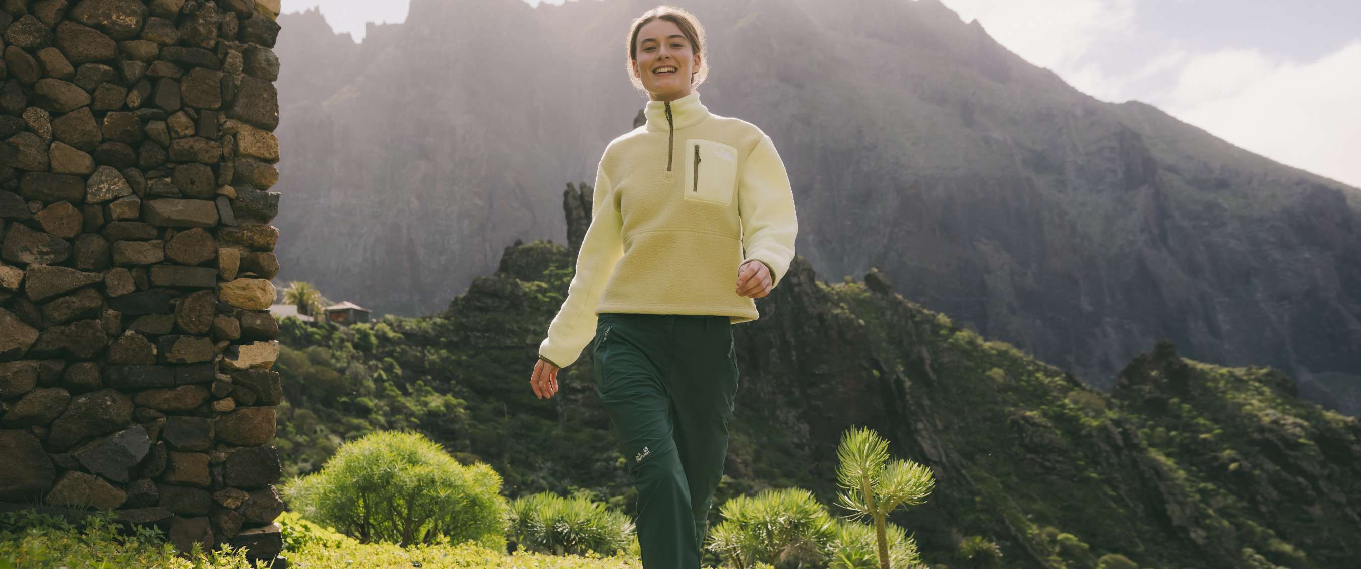 Femme marchant dans un paysage de montagne avec une polaire claire et un pantalon de randonnée vert