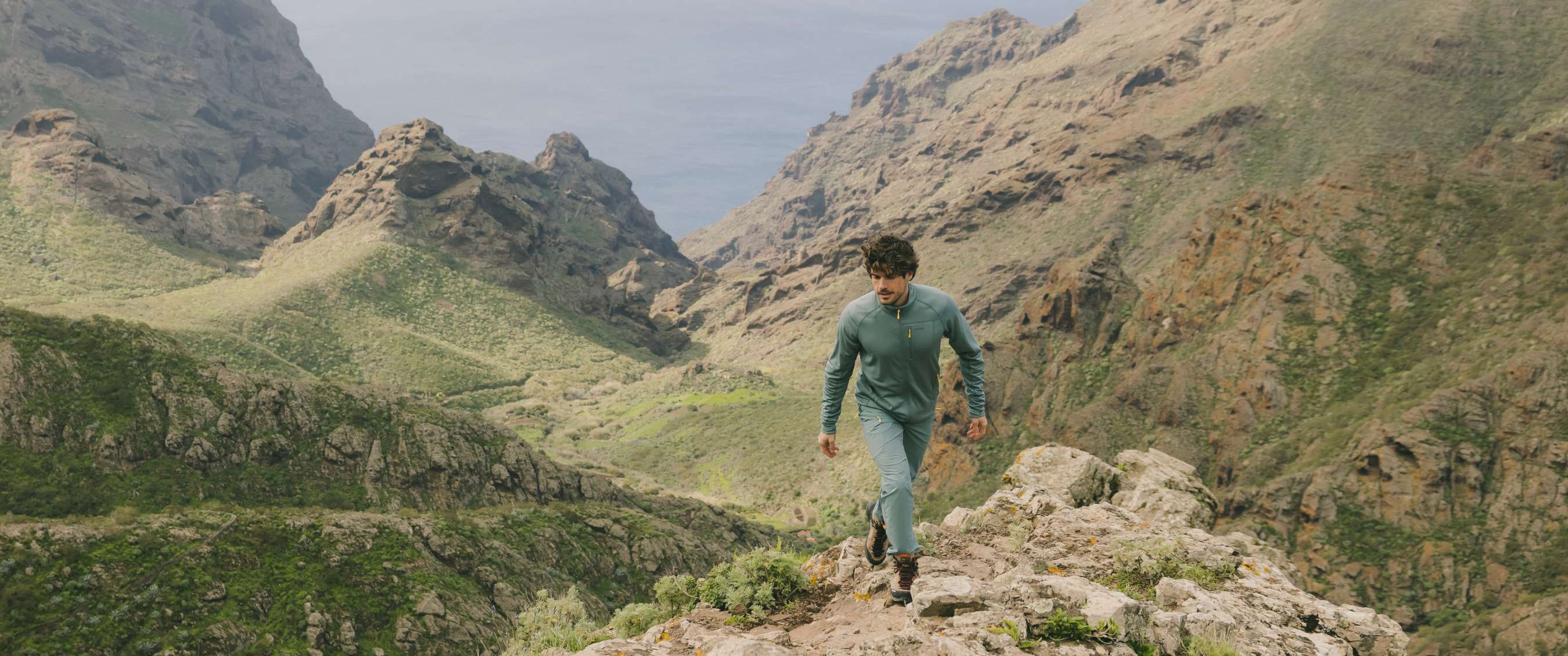 Homme sur un sentier de montagne avec vue sur la mer entre des parois rocheuses
