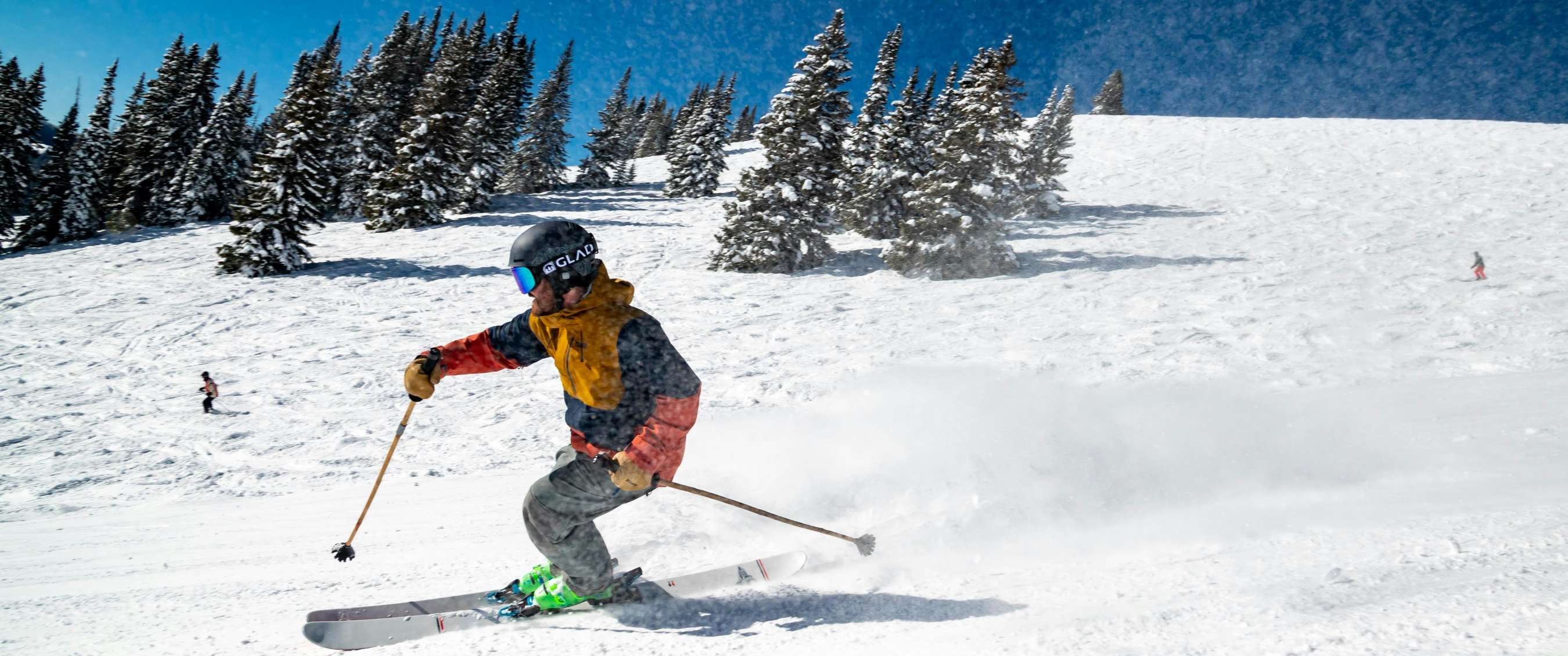 Personne sur des skis projetant de la neige lors d’une descente rapide sous un ciel ensoleillé.